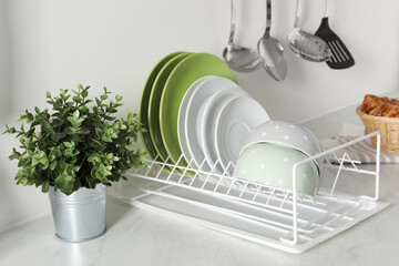 Wall Mural - Drainer with different clean dishware and houseplant on light table in kitchen