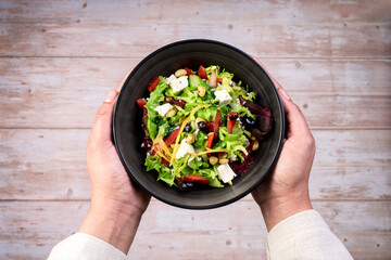 Wall Mural - Female hands holding bowl with green lettuce salad vegetable salad, top view. 