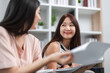 © wichayada - Young Female Friends Collaborating and Helping Each Other Study for Exam in a Modern Home Environment