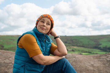 Woman Wearing Orange Knit Hat Sits on Hilltop Looking Out Over the Landscape