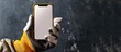 © vxnaghiyev - Foreman holding a phone displaying a blank screen in a hand wearing gloves, designed for showcasing home repair or construction projects with copy space image.