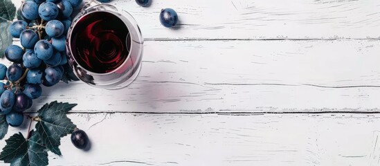 Poster - Red wine glass and blue grapes with leaves on white wooden table with copy space image.