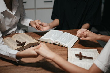 Wall Mural - Group of Christians sit together and pray around a wooden table with blurred open Bible pages in their homeroom.