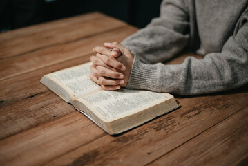 Wall Mural - Group of Christians sit together and pray around a wooden table with blurred open Bible pages in their homeroom.