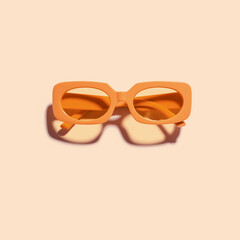 Trendy sunglasses with orange Frame on peach color background, copy space, beach vibes, summertime mood, sunlight shadow and glare, summer fashion vivid glasses. Minimal top view of eyeglasses