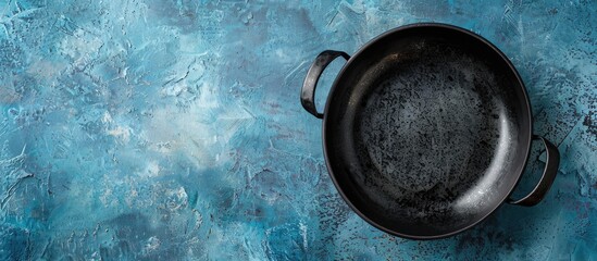 Poster - Bird's eye view of a vacant black ceramic bowl with two handles set against a blue concrete backdrop, providing ample copy space image.