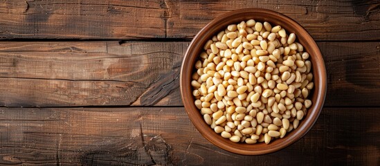Poster - Top view of a bowl with pine nuts on a wooden background, providing space for a text overlay or other elements in the image. copy space available