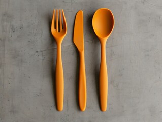 Wall Mural - Orange plastic cutlery set on gray background, featuring fork, knife, and spoon. Modern design for kitchen or dining. Vibrant orange color adds excitement to mealtime. Flat lay shows sleek look