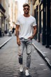 © Vit - A fashionable man confidently poses in ripped jeans and a classic white t-shirt, showcasing a trendy street style look. The distressed denim and casual top create a stylish yet laid-back aesthetic