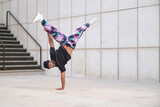 Young man is breakdancing on the street in front of a wall