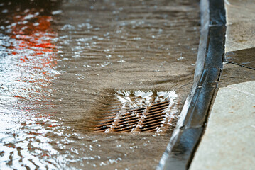 rainwater flowing over highway storm drain grate. floodwater and drainage on roads during heavy rain