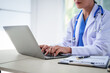 © NanSan - An Asian female doctor sits at her desk, conducting an online consultation. This faster, cheaper, and more convenient method helps prevent disease spread and offers easier access to healthcare.