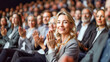 © Pavel Lysenko - A woman with blonde hair smiles as she claps with the crowd at a business event or conference