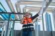 © Washburn - A construction engineer in a safety vest and helmet inspects industrial pipes on a rooftop while communicating via walkie-talkie.