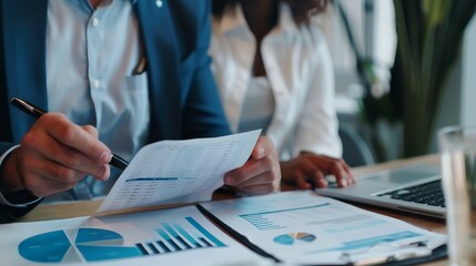 Poster - Businessman Reviewing Financial Reports with a Colleague - A businessman analyzes financial reports with a pen while a colleague works on a laptop, creating a professional atmosphere. - A businessman 