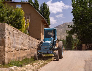 A blue tractor is parked on a dirt road in front of a house