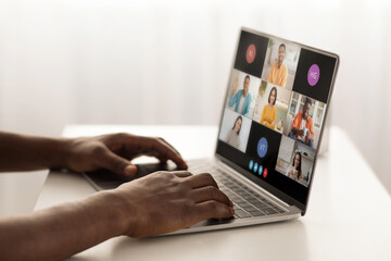 Poster - A person is sitting at a desk, using a laptop to participate in a video conference with several other people. The laptop screen displays a grid of video windows, each showing a different participant