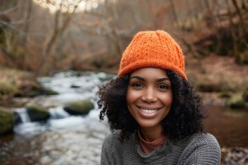 Wall Mural - Portrait of a grinning afro-american woman in her 40s sporting a trendy beanie on tranquil forest stream