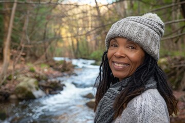 Wall Mural - Portrait of a grinning afro-american woman in her 40s sporting a trendy beanie in front of tranquil forest stream