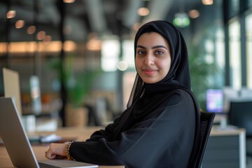 Happy Arab woman in abaya looking at front camera with laptop computer Blurred notebook and office