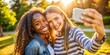 © Man888 - Vibrant smartphone screen displaying selfie of two beaming teenage girls from different racial backgrounds embracing joyful friendship and togetherness in a sunny outdoor setting.