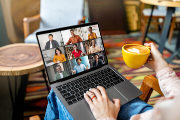 Poster - A person sits in a cafe with a laptop open, attending a video conference. They have a cup of coffee in their other hand. The laptop screen shows multiple video squares of other participants.