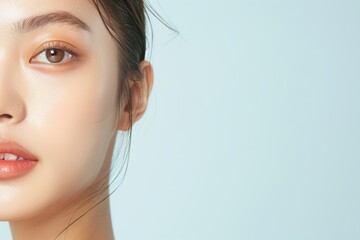 Close-up of a woman's face with natural makeup and soft lighting, showcasing clear skin and a serene expression against a light background.