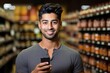 © sorin - Smiling man shopping, using phone app for groceries, making eye contact while in a supermarket aisle