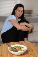 Canvas Print - Eating disorder. Sad woman on sofa indoors, focus on granola, kiwi and banana