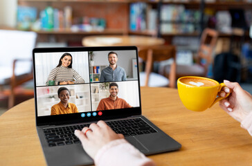 Poster - A person sits in a cafe, using a laptop to video conference with three colleagues. They are smiling and engaged in conversation, enjoying a cup of coffee. The cafe is cozy and relaxed