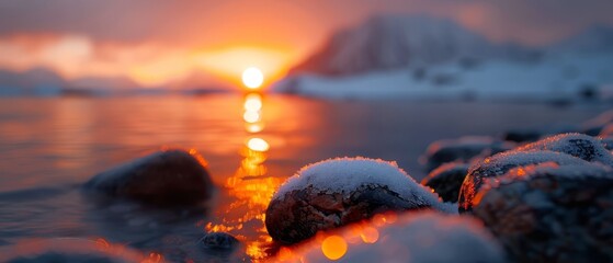  Sun sets over water, foreground dotted with rocky outcrops and dusted with snow