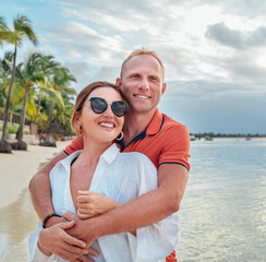 Wall Mural - Couple in love hugging on the sandy exotic beach while they have a evening walk by the Trou-aux-Biches seashore on Mauritius island. People relationship and tropic honeymoon vacations concept image.