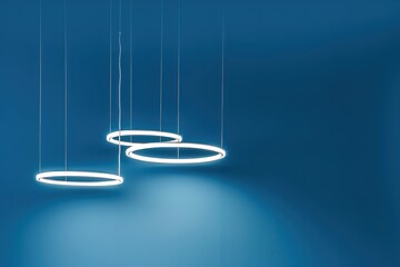 Wall Mural - Blue background, circular lighting suspended from the ceiling in three different positions, with white light inside each ring and white cables hanging down.