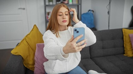 Poster - Young redhead woman taking a selfie on a smartphone in a cozy living room setting.