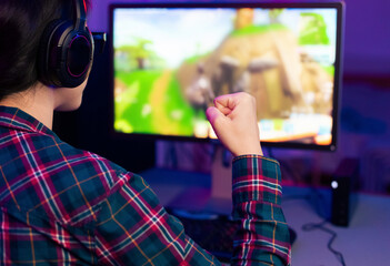 Aufkleber - A young gamer, wearing headphones and a plaid shirt, raises their fist in celebration, seemingly victorious in a video game displayed on the computer monitor.