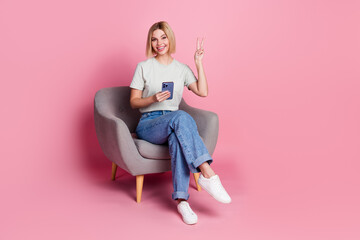 Wall Mural - Photo of cheerful lovely nice girl wear stylish grey clothes sit chair hold device v-sign isolated on pink color background