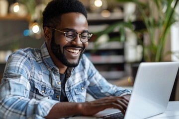 Beautiful African man with a well-groomed beard, wearing glasses, smiling and laughing while using a laptop to shop online with his credit card from the comfort of his home.