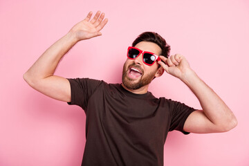 Wall Mural - Photo of positive man with stylish bristle dressed brown t-shirt touch sunglass dancing in night club isolated on pink color background