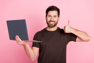 Poster - Portrait of satisfied pleasant man wear brown shirt hold laptop showing thumb up approve good work isolated on pink color background