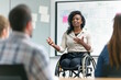 © MarGa - African American woman in wheelchair giving a presentation to colleagues. Office meeting, team discussion, workplace inclusion. Concept for leadership, teamwork, International Day of Persons with Disa