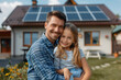 © S photographer - A Caucasian family hugs in front of a house powered by solar panels.