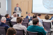 © Anton Gvozdikov - Group of professionals attentively listening to a speaker at a tech conference, focusing on a presentation. Blurry view of the speaker at the podium.