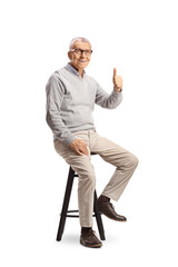 Sticker - Cheerful elderly man sitting on a chair and gesturing thumbs up