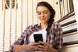 © wavebreak3 - Using smartphone, young woman sitting on stairs and smiling at home