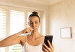 © WavebreakMediaMicro - Brushing teeth, woman using smartphone and looking at screen in bathroom