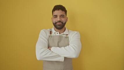 Sticker - Happy young hispanic man wearing apron, standing with crossed arms against an isolated yellow background, emanating positive vibes with a vivacious smile