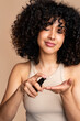 © mahalo studio/Stocksy - woman with curly hair applying oil