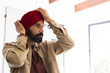 © Wavebreak Media - Adjusting red turban, man standing indoors, focusing on traditional attire, copy space