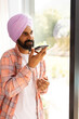 © Wavebreak Media - Speaking on smartphone, Indian man in turban standing by window at home