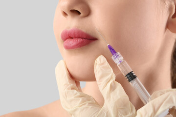 Poster - Young woman receiving filler injection in face on grey background, closeup